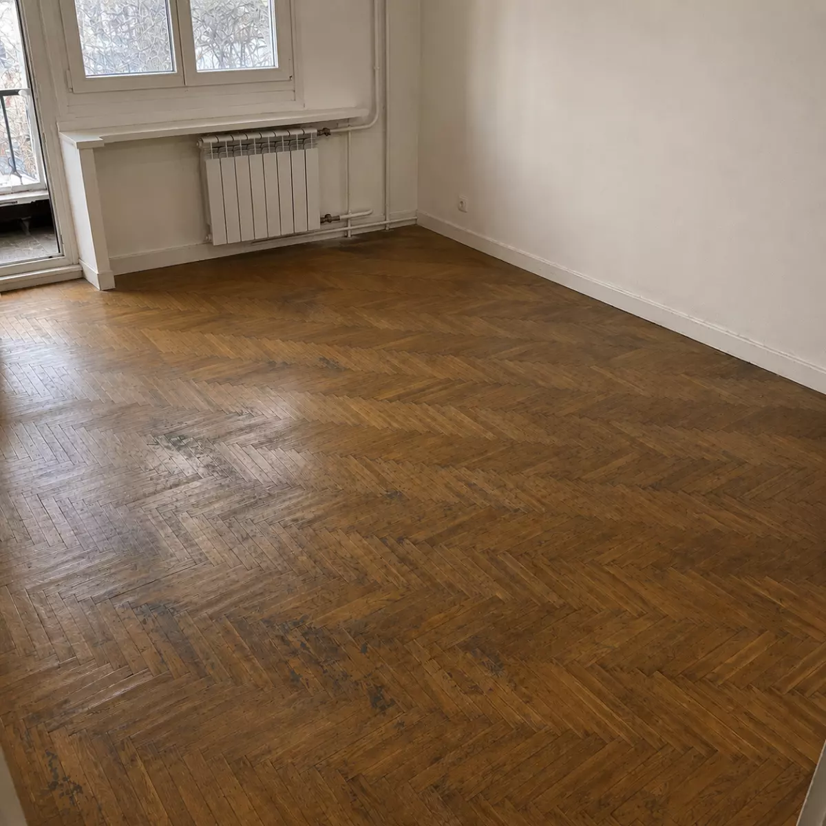 Pièce avec parquet en chevrons avant rénovation, finition ternie et irrégulière