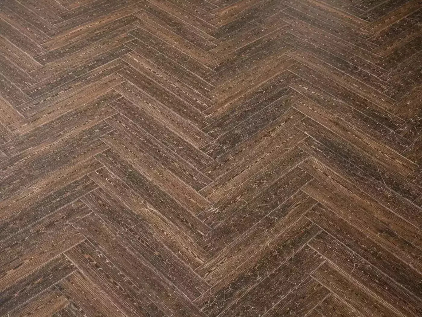 Détail d'un parquet en chevrons avant ponçage, finition foncée et encrassée